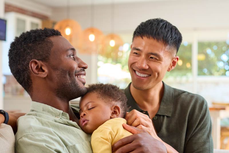 Two fathers holding daughter, feeling financially secure.