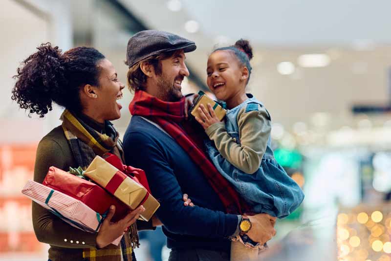 Family of shoppers carrying gifts, highlighting holiday spending with a KEMBA Visa credit card.