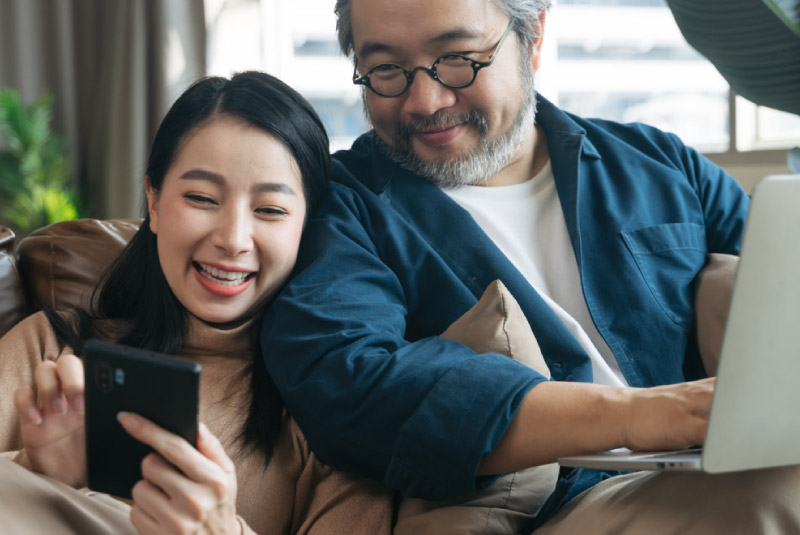 smiling father and daughter using computer and smartphone to bank online