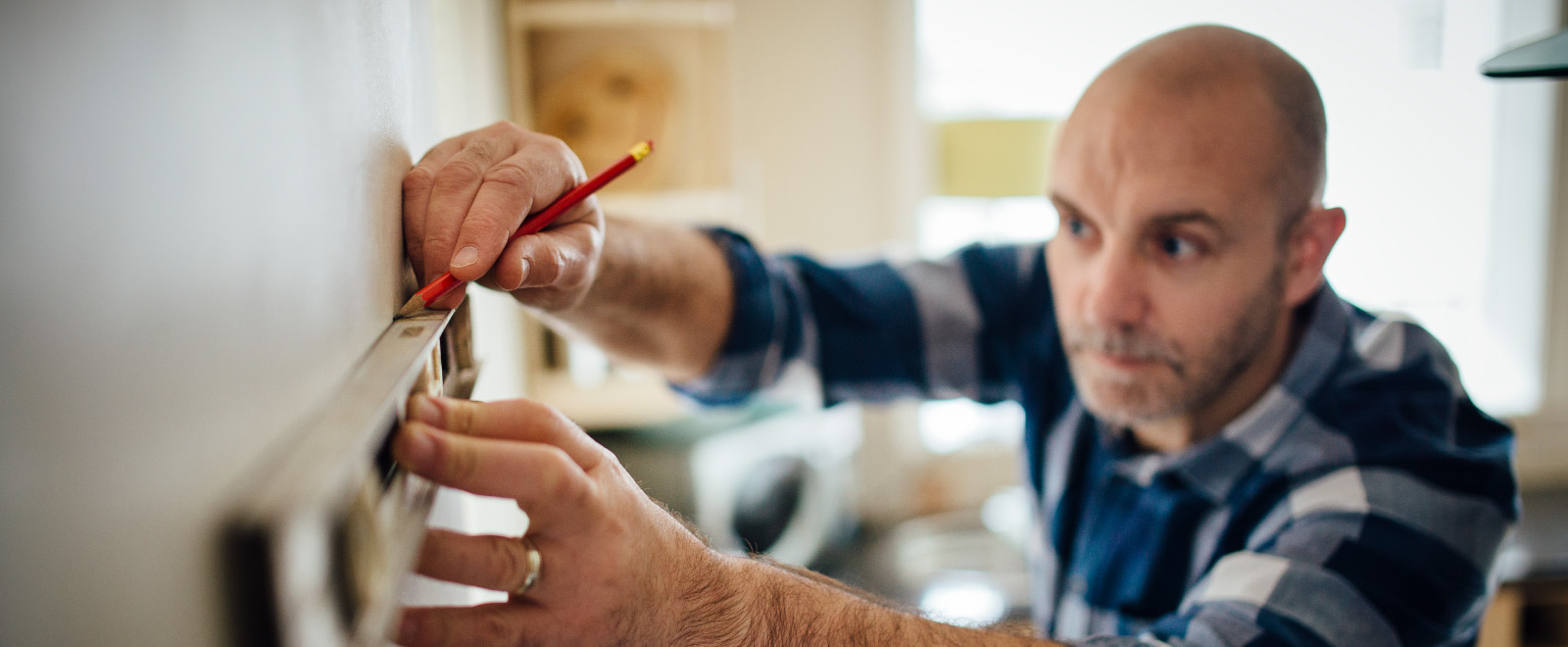 A man using a leveler and making a mark on a wall with a pencil.