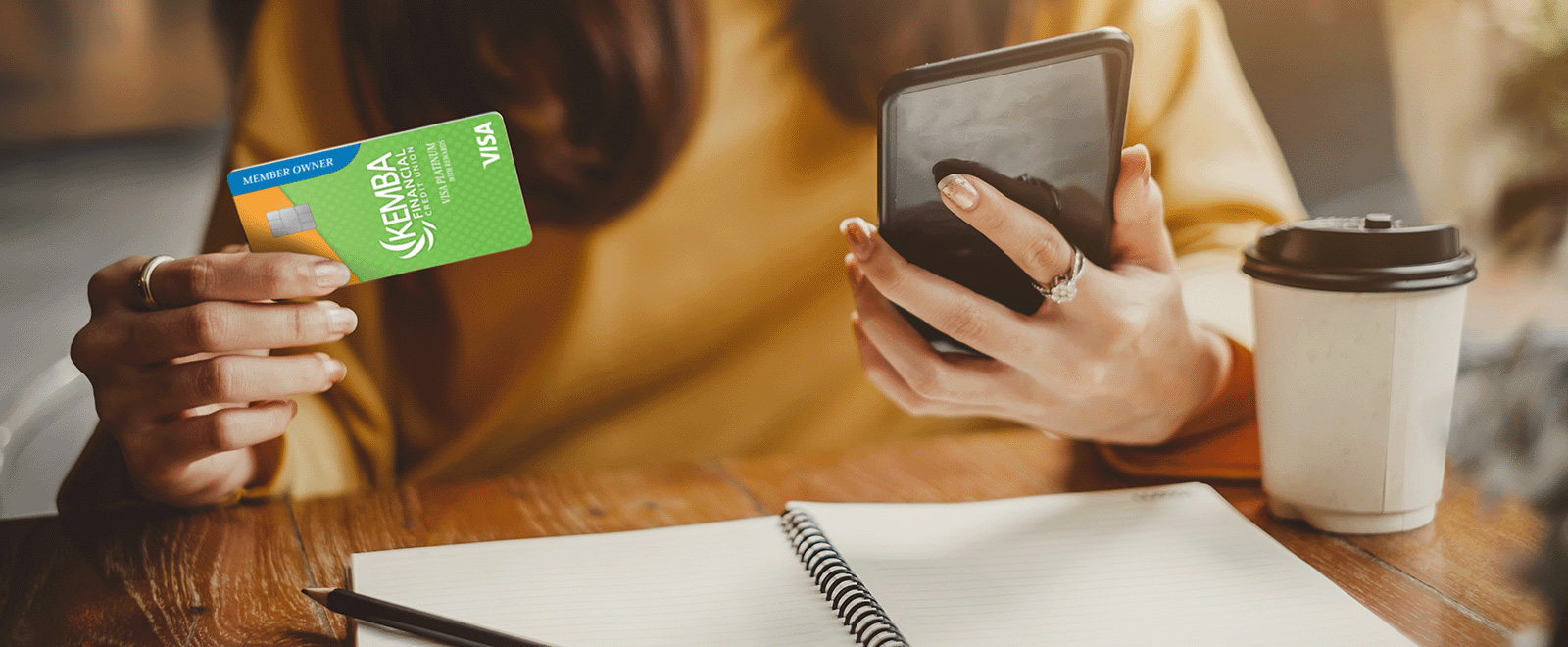 Person holding a KEMBA Visa Platinum Credit Card in one hand and a smartphone in the other