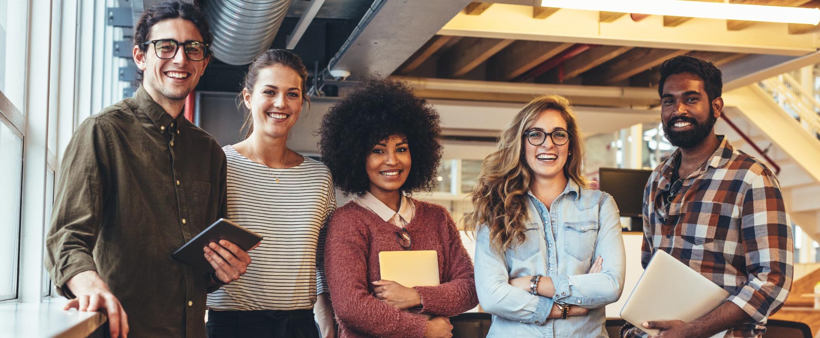 A group of five people standing and smiling in an industrial office.