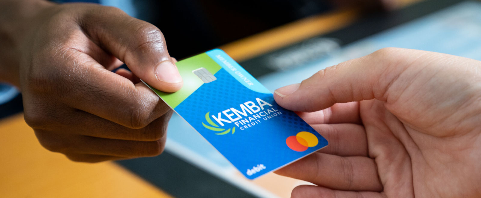 KEMBA teller handing KEMBA debit card to new member