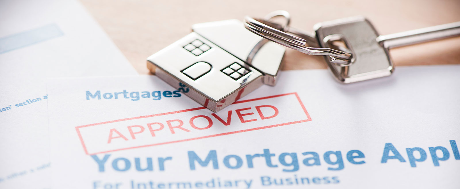 A house keychain with a key on an approved mortgage loan paper.
