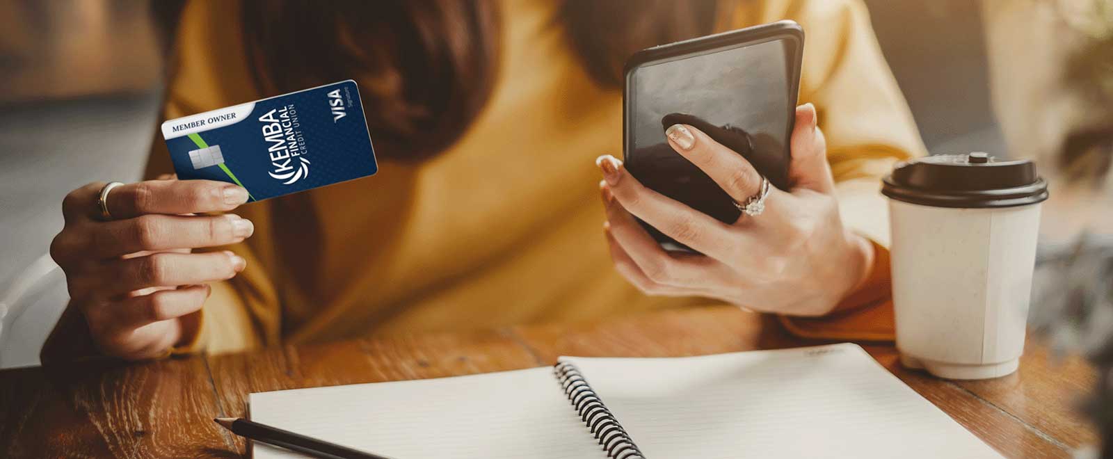 Person holding a KEMBA Visa Signature® Credit Card in one hand and a smartphone in the other