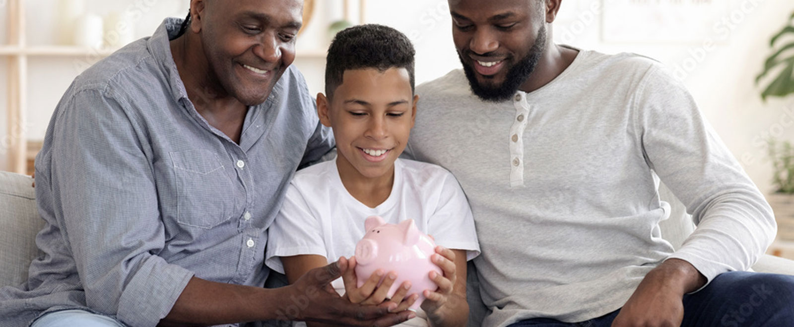 A young boy in between his dad and grandfather holding a piggy bank.