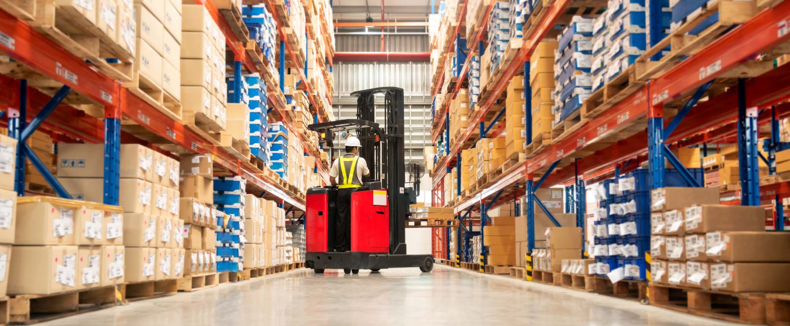 A man with a hard hat and vest operating a fork lift in a warehouse.