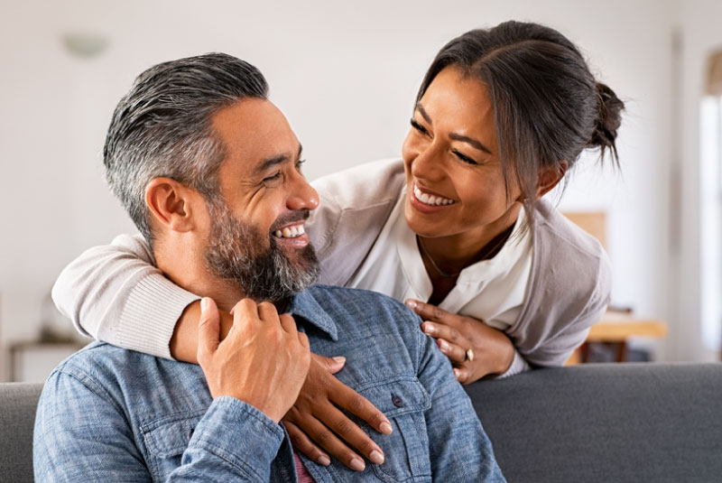 A couple smiling at one another with the woman's arm around the man.