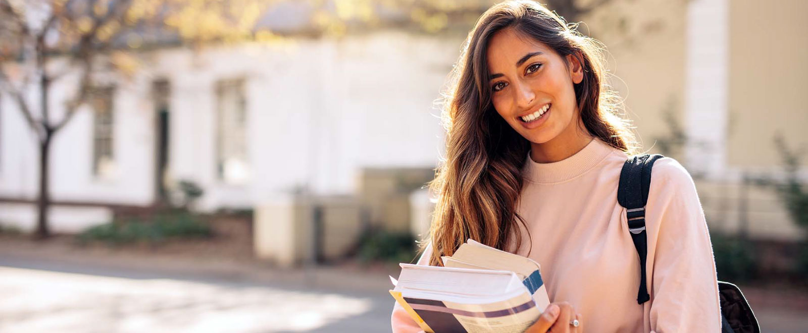 college age woman smiling and carrying books