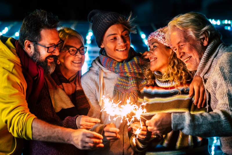 A group of five people standing together outside and holding sparklers.