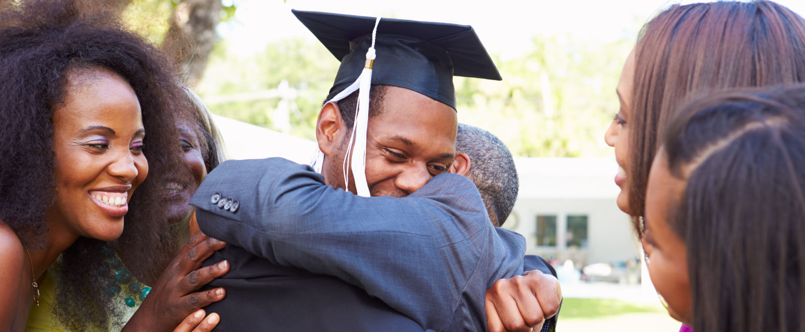 A man in a graduation gown and cap with his family surrounding him and hugging him.