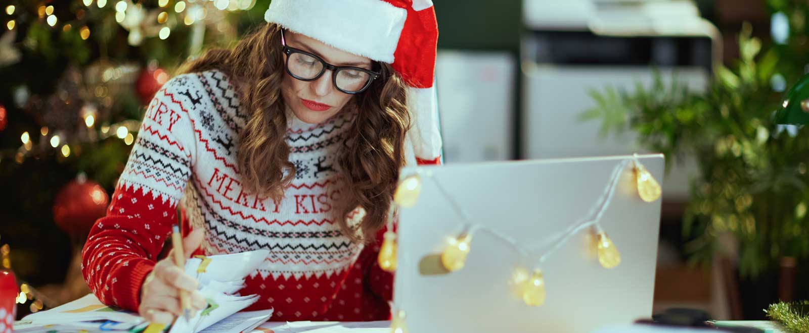 A woman wearing glasses dressed in Christmas apparel looking through papers.