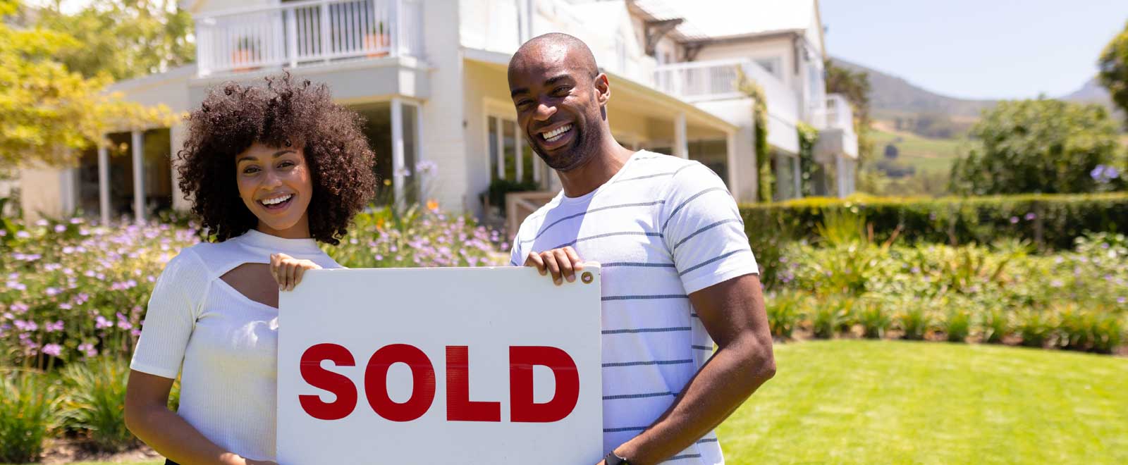 A couple standing in front of a house holding a "sold" sign.
