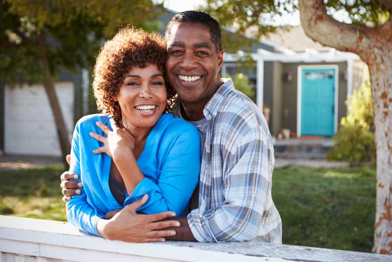 A couple smiling and holding one another in front of a house.