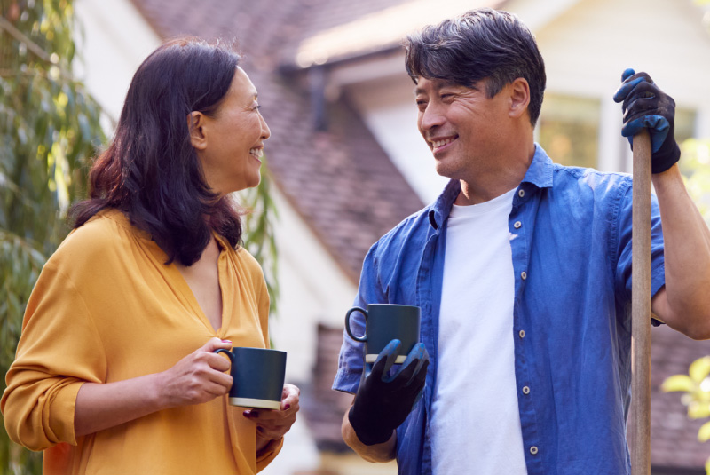 A man and a women holding a mug smiling at each other in a yard doing work.