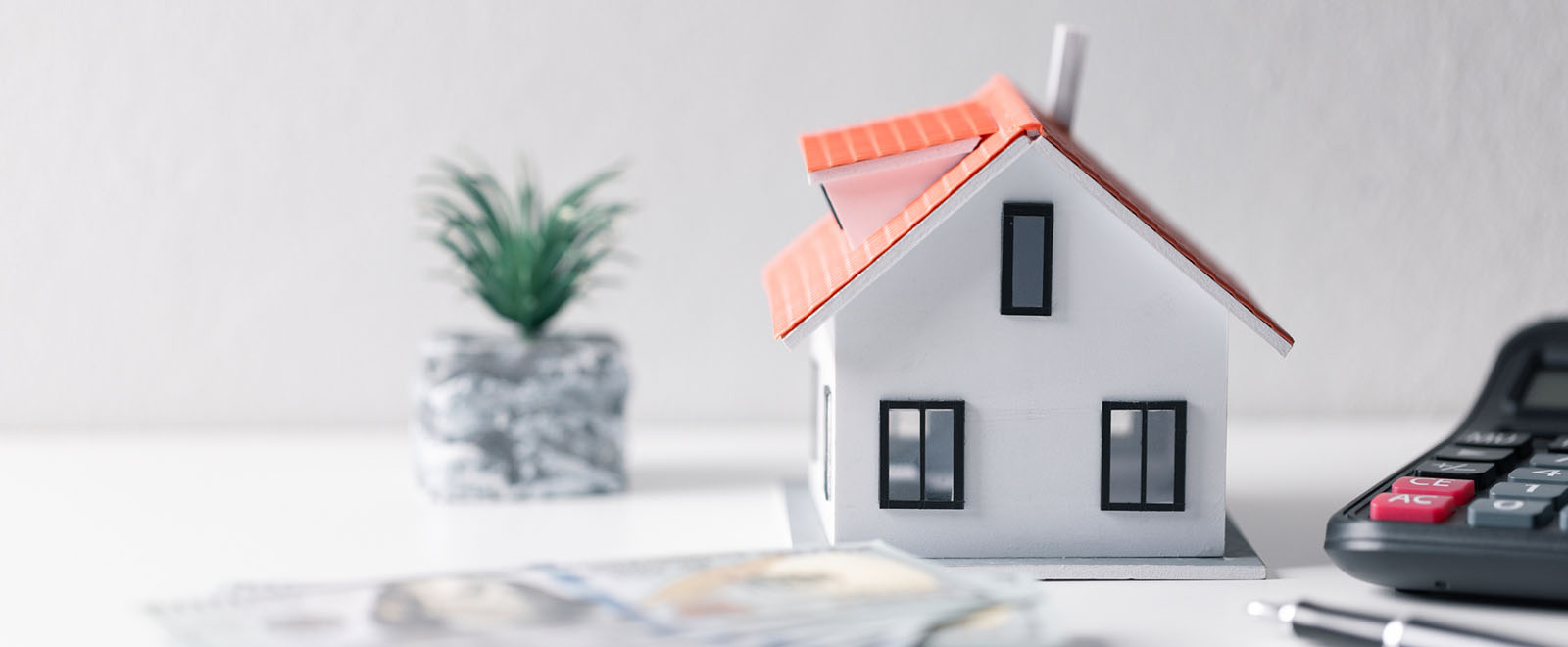 Small model house with money in front and a calculator