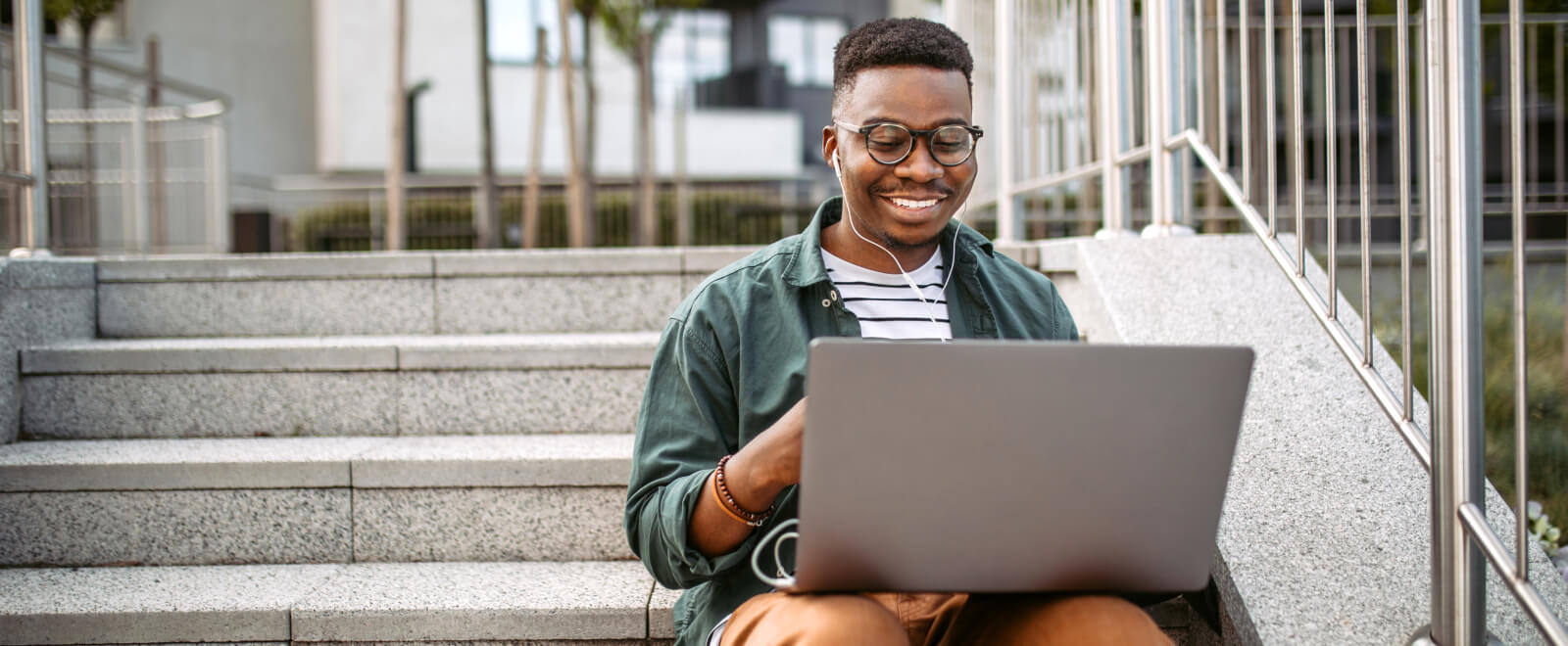 Young male student on computer sitting on steps outdoors .