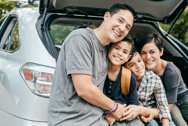 A family of four sitting in an open trunk smiling.
