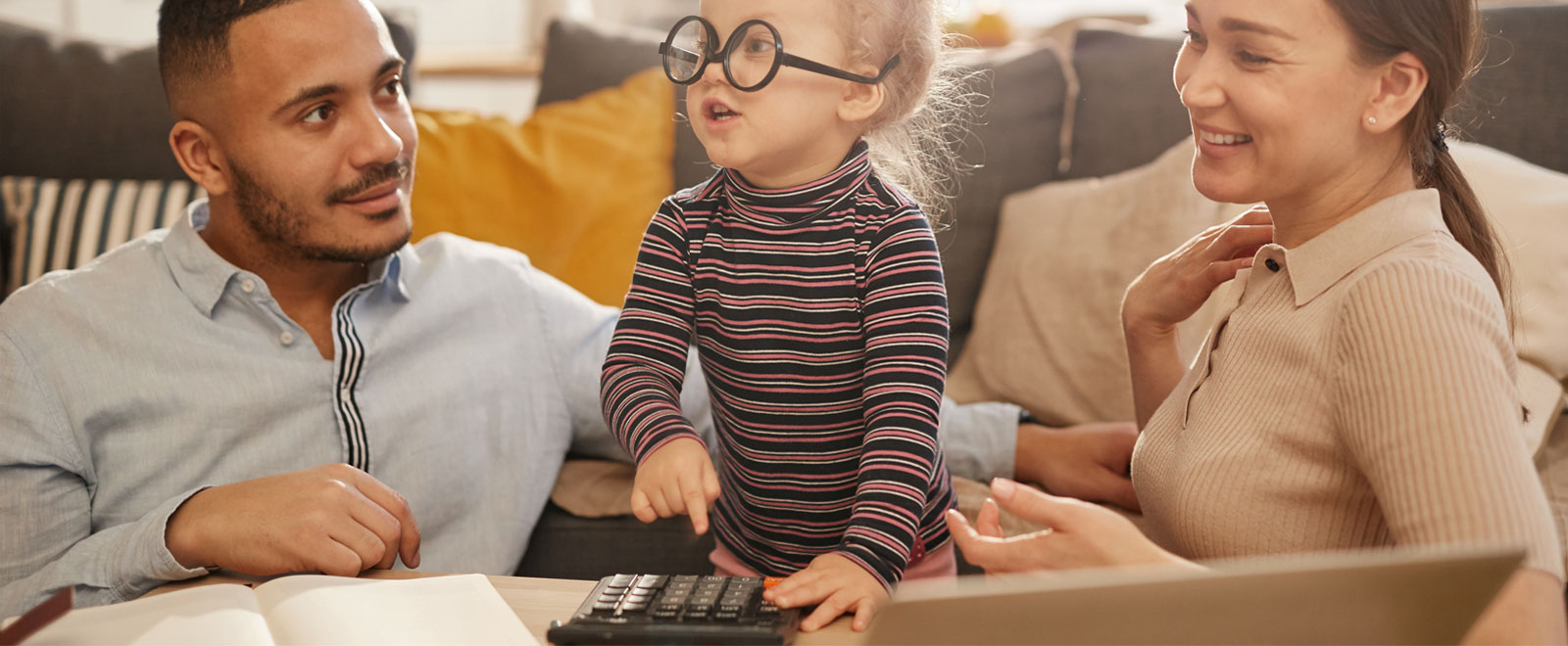 A young girl wearing upside down glasses standing in between her two parents that are looking at her.